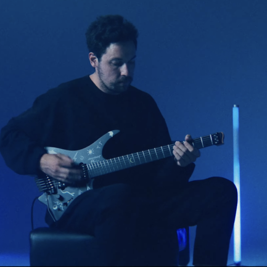 Plini playing his Strandberg Boden Standard NX 6 Plini Edition Mirage signature electric guitar under blue stage lighting.