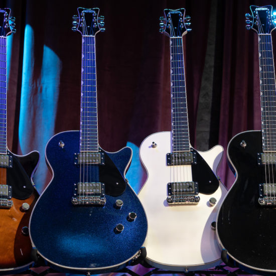 Four Gretsch Electromatic Premier Jet electric guitars in different finishes displayed on stands against a stage curtain backdrop.